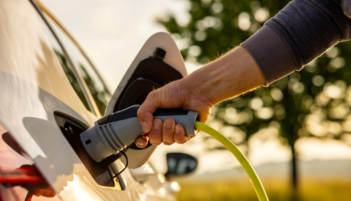 Man inserts a power cord into an electric car for charging in the nature